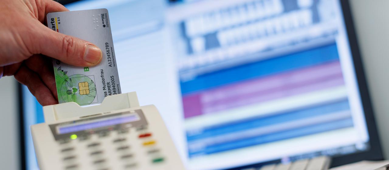 Eine Frau steckt eine Krankenkassenkarte in ein Lesegerät in einer Arztpraxis.