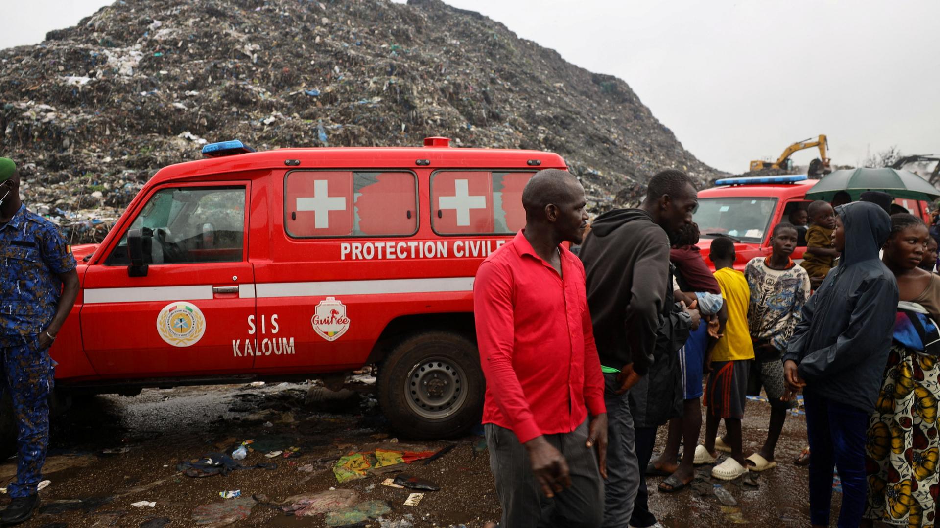 Menschen stehen vor roten Rettungswagen auf einer Mülldeponie in Guinea | REUTERS