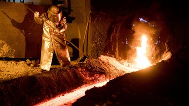 Arbeiter steht in einem Stahlwerk vor einem Hochofen