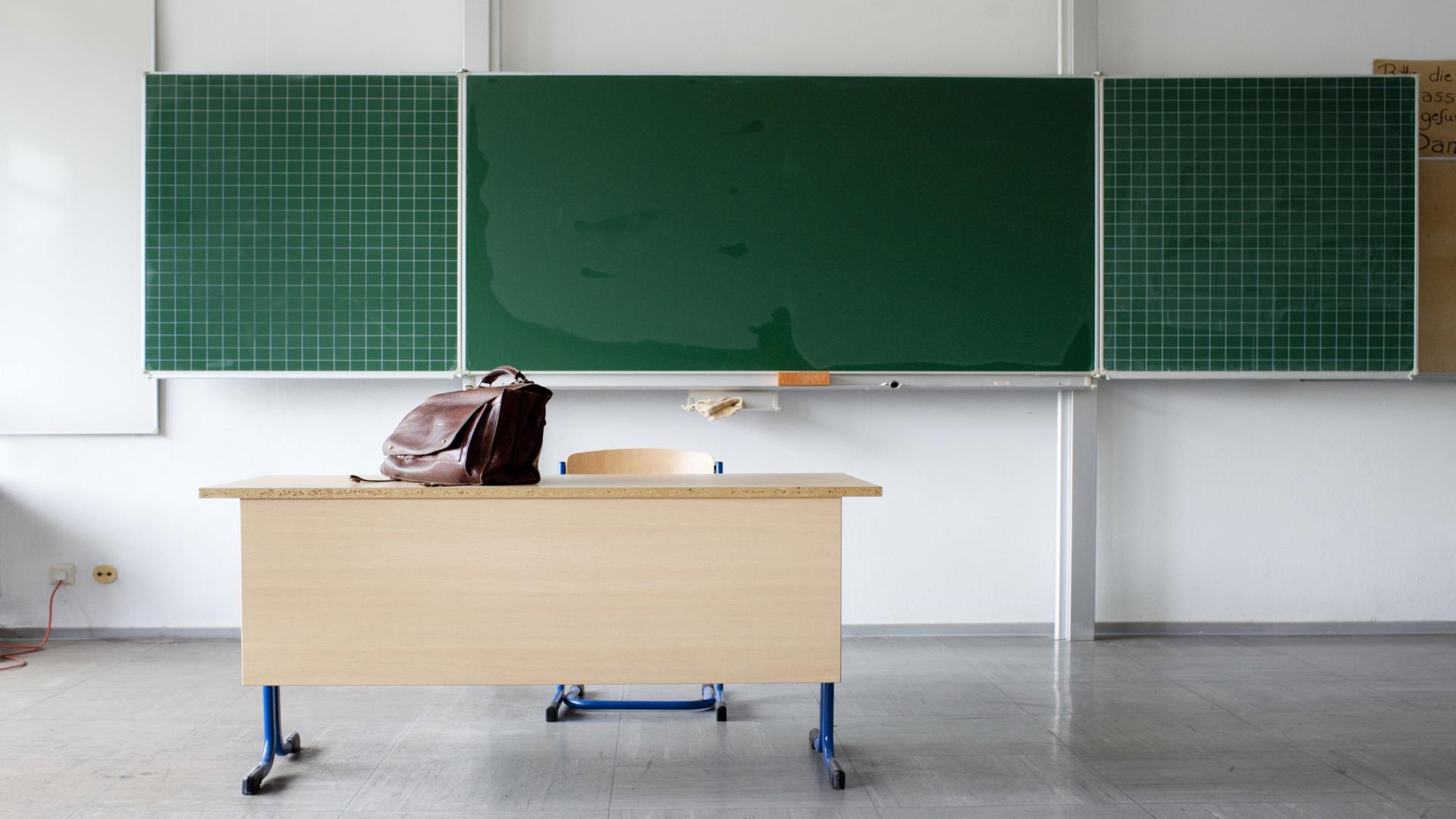 Schultafel in einer Klasse und davor steht ein Pult auf dem eine Tasche steht | WDR