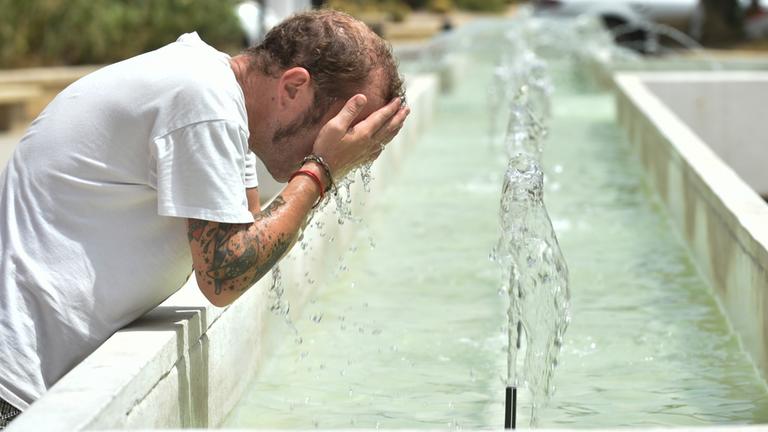 Ein Mann kühlt sich an einem Brunnen