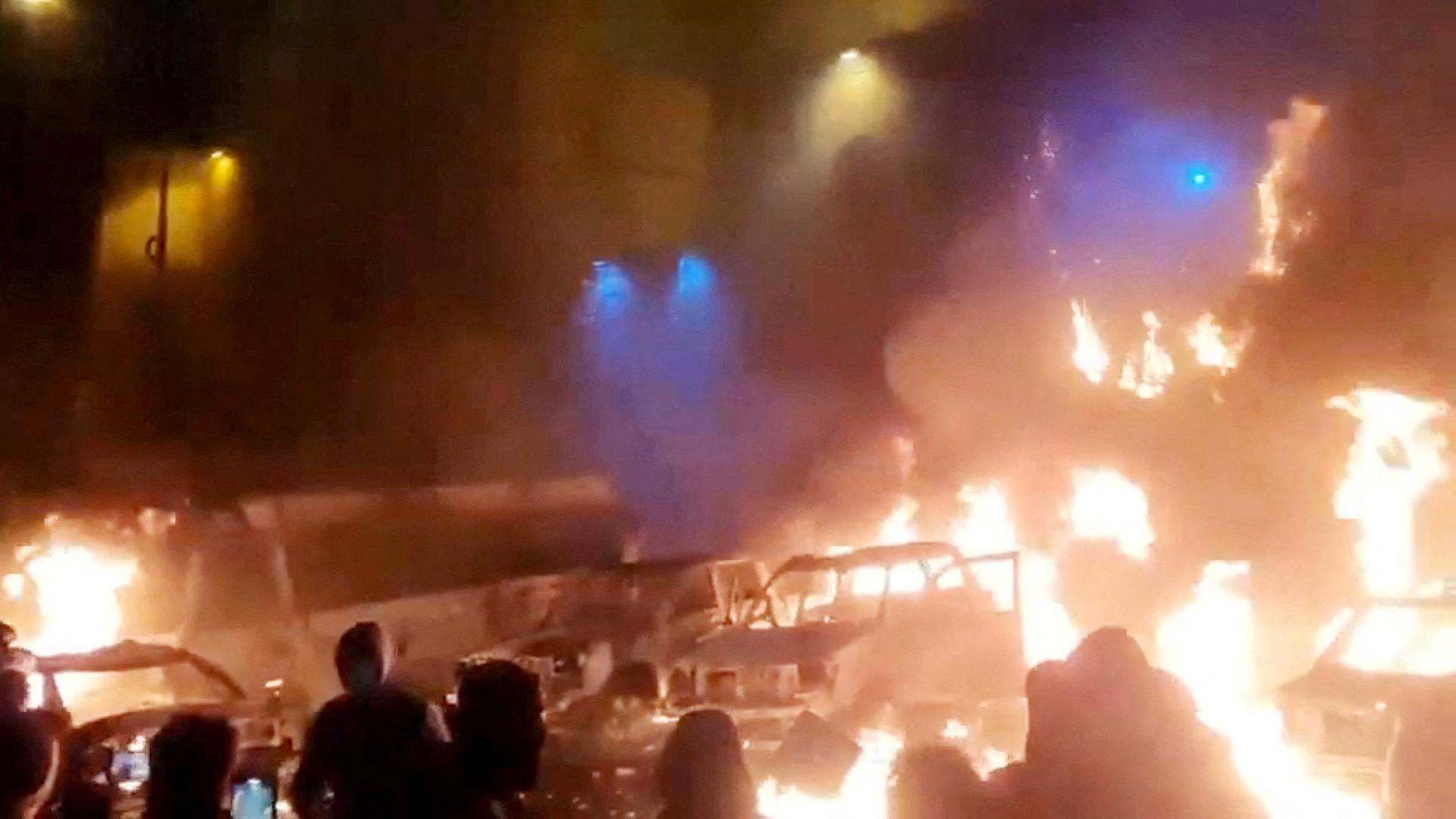 Menschen stehen vor brennenden Autos in der Nacht | via REUTERS