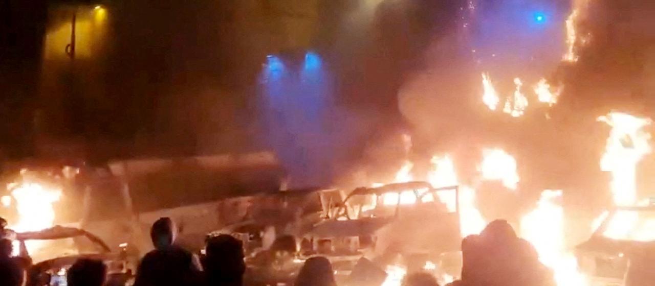 Menschen stehen vor brennenden Autos in der Nacht