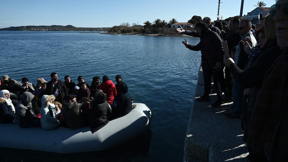 Migranten in einem Boot in einem Hafen der griechischen Insel Lesbos, gestikulierende Einwohner am Kai