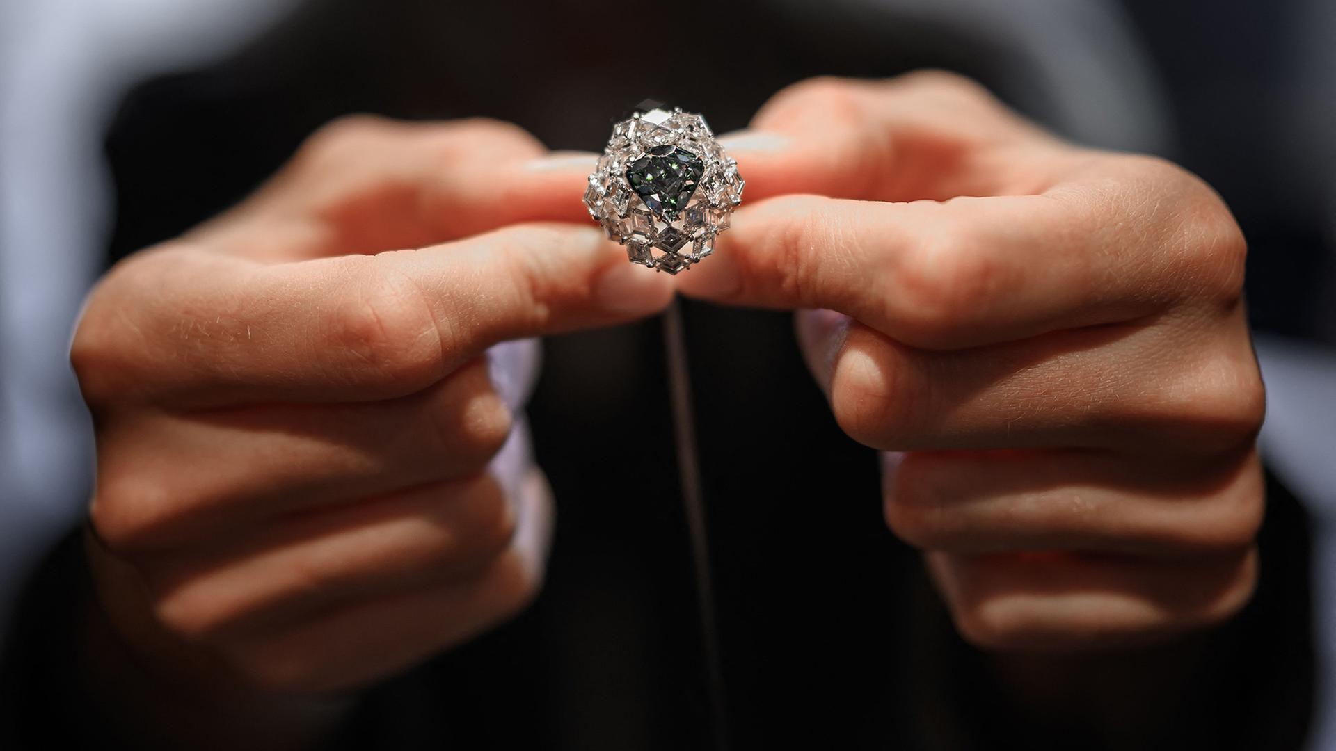 Ein Mitarbeiter von Christie’s präsentiert in Genf einen dreieckigen, leuchtend blaugrünen Fancy-Diamanten. | AFP