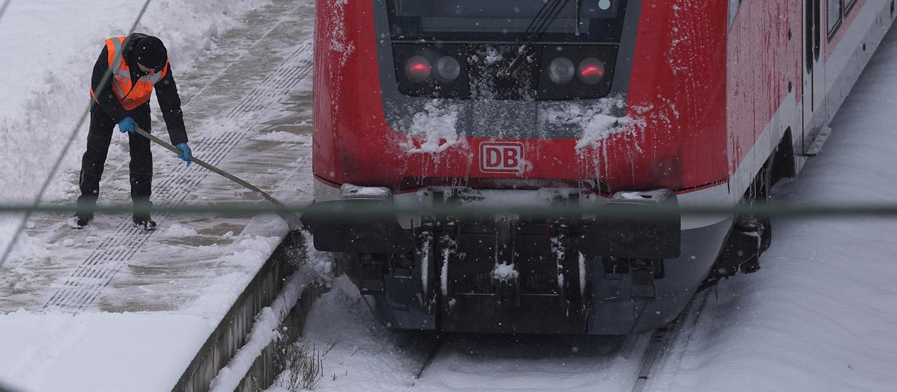 Ein Mitarbeiter beseitigt eine dicke Schneeschicht auf einem Bahnsteig.
