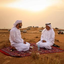 Männer sitzen auf einem Teppich in einer Wüste.