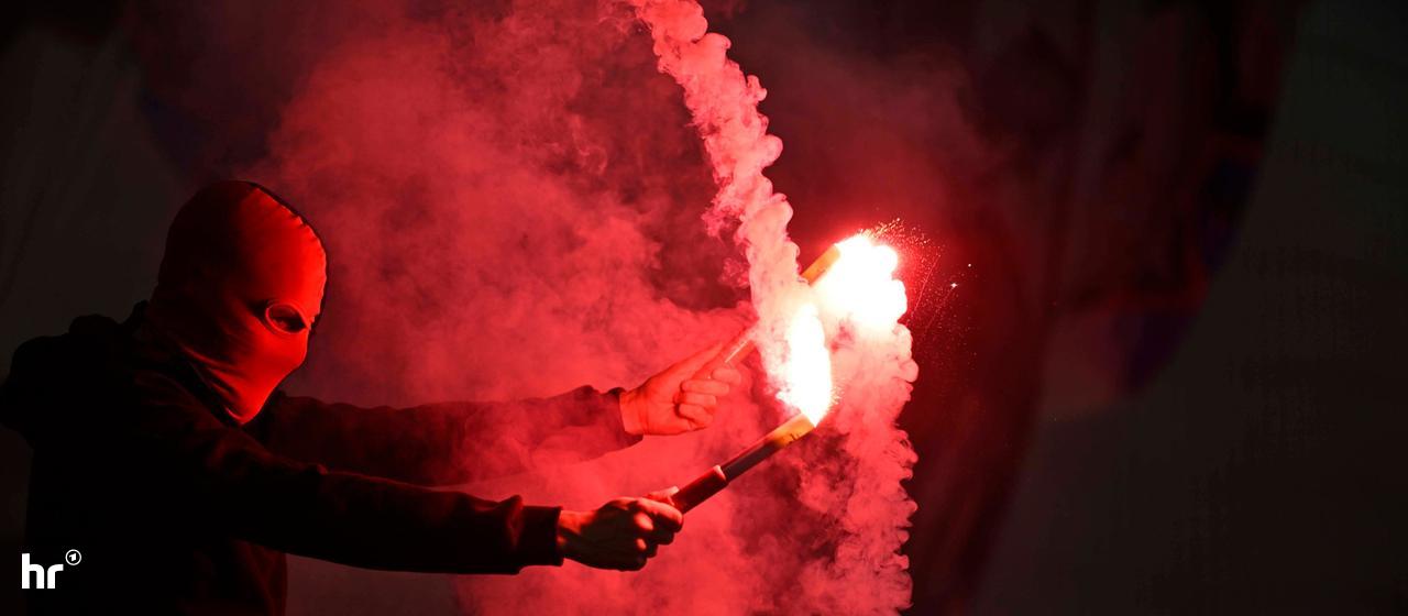 Zwei Hände halten rote Bengalo-Fackeln - von Qualm umgeben