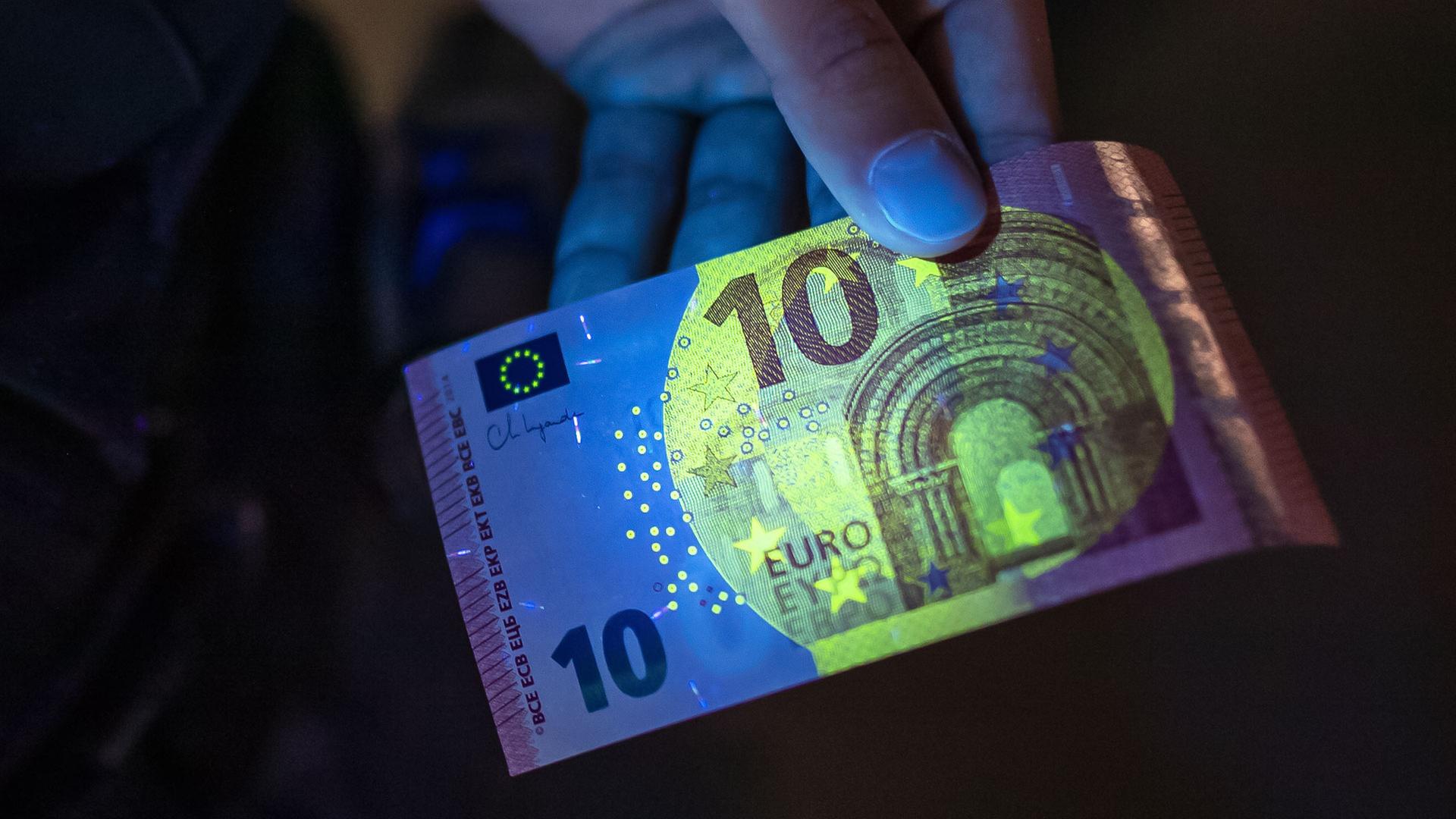 Ein Polizist überprüft mit Hilfe von UV-Licht die Echtheit eines Geldscheins. | picture alliance/dpa