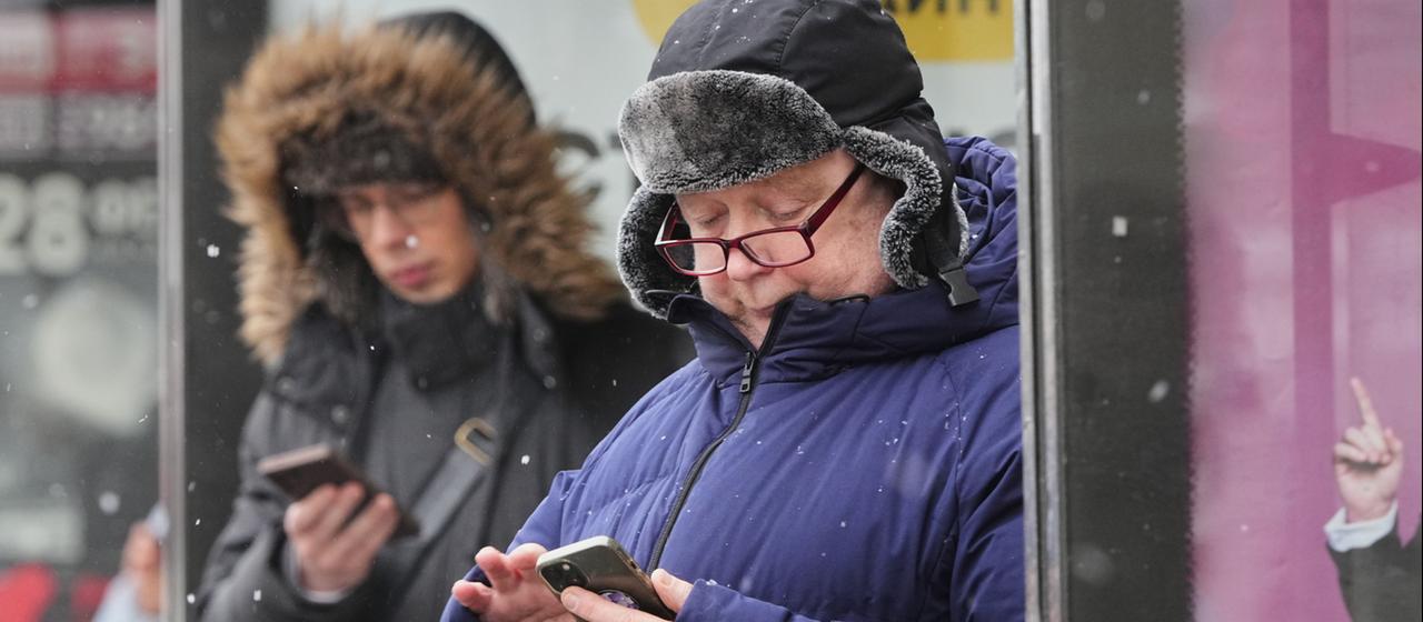 Menschen warten an einer Bushaltestelle und schauen auf ihr Smartphone.