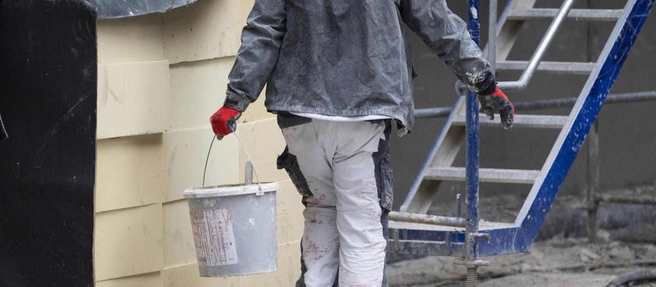 Ein Bauarbeiter trägt einen Eimer über eine Baustelle.