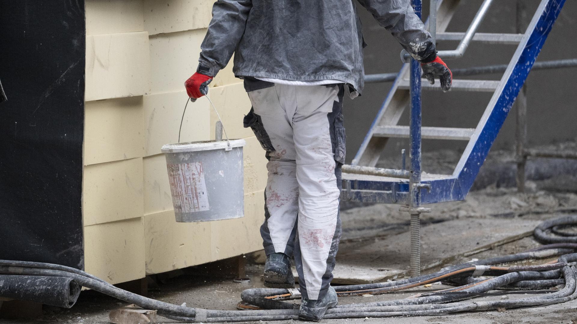 Ein Bauarbeiter trägt einen Eimer über eine Baustelle. | dpa