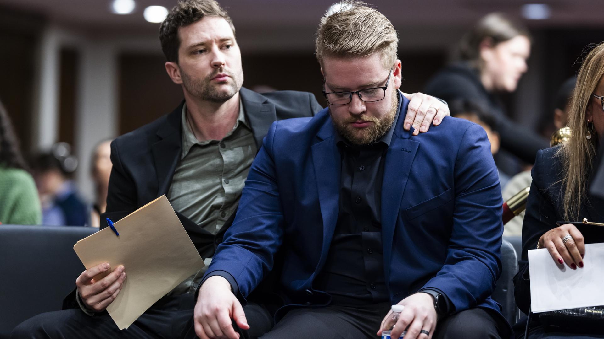 Brent und Luke Ganger sitzen auf Stühlen, Luke hält den Kopf gesenkt, sein Bruder hat einen Arm um seine Schultern gelegt. | EPA