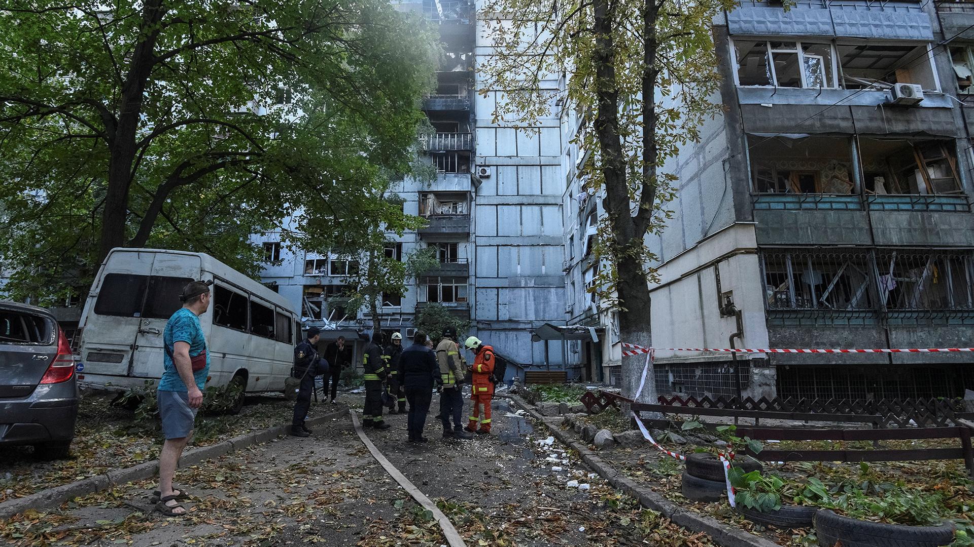 Feuerwehrleute stehen vor einem zerstörten Haus. | REUTERS