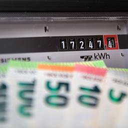 Euro-Geldschein werden vor einem Stromzähler im Privathaushalt gehalten.