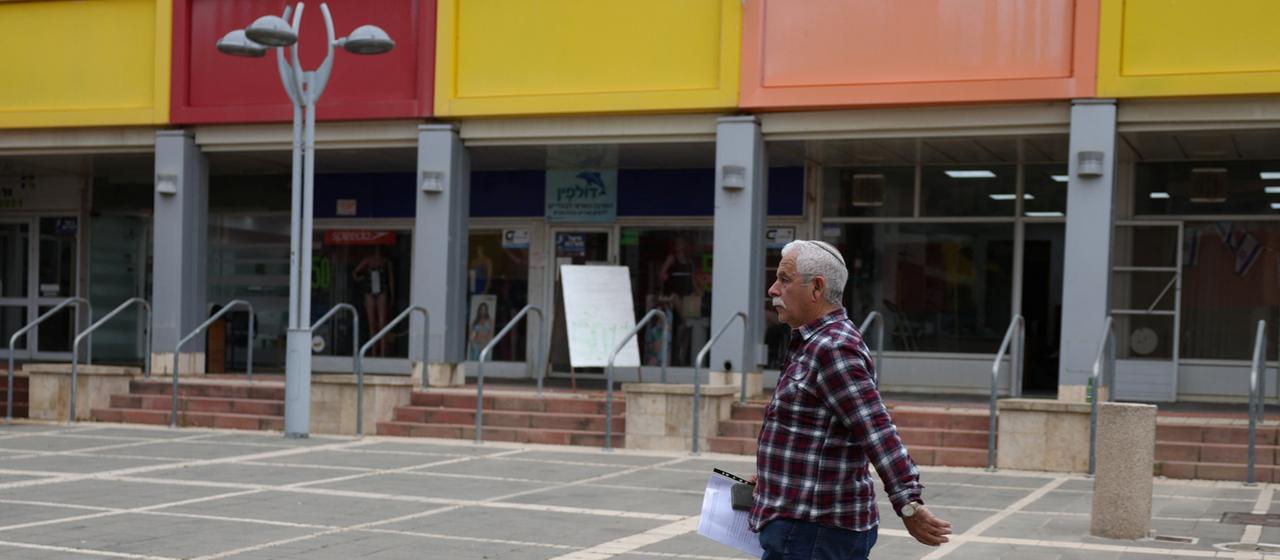 Ein Mann läuft in Kiriat Schmona an einer Ladenzeile mit dunklen Schaufenstern vorbei.