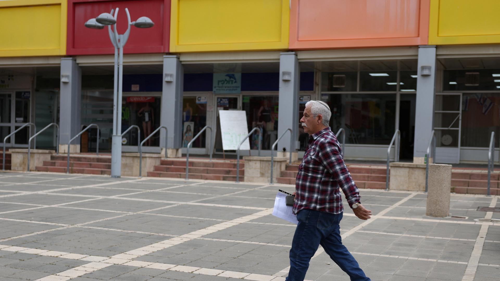 Ein Mann läuft in Kiriat Schmona an einer Ladenzeile mit dunklen Schaufenstern vorbei. | REUTERS
