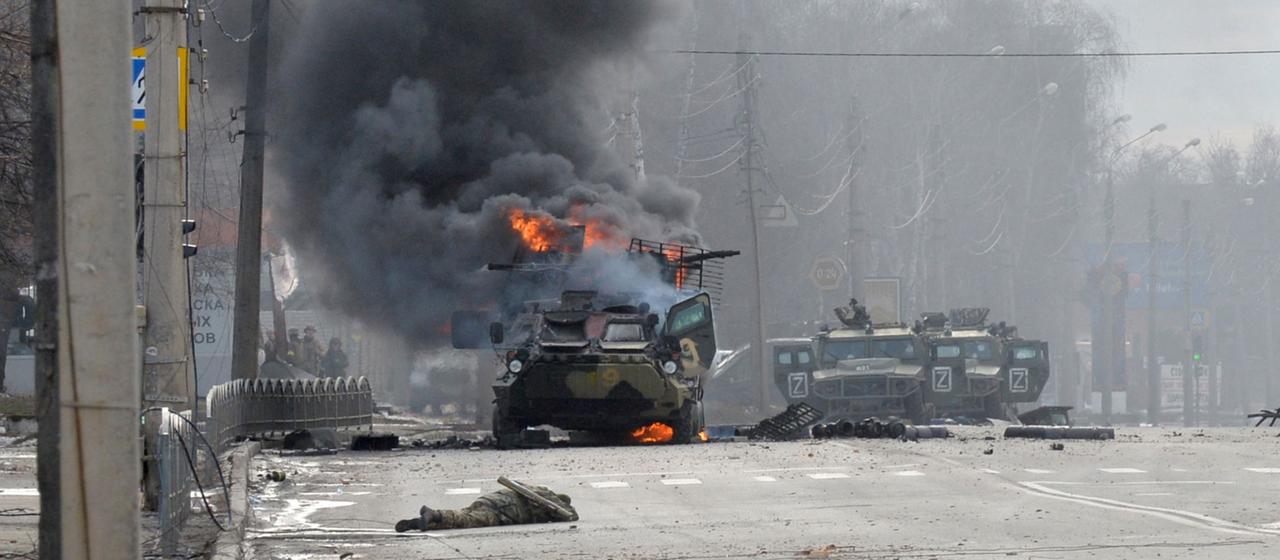Eine Leiche liegt vor einem brennenden russischen Militärfahrzeug in Charkiw, Februar 2022.