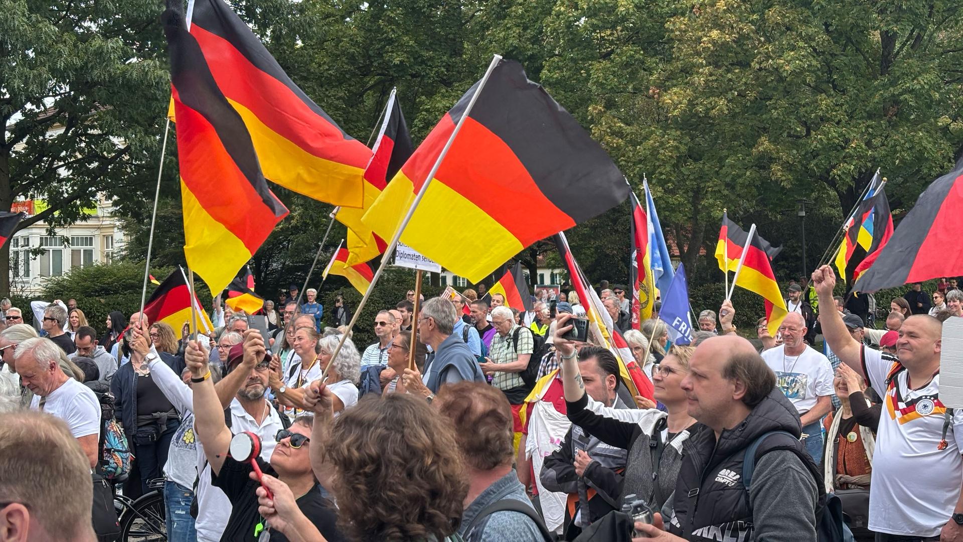 Mehrere Menschen haben sich für eine Demo versammelt, einige halten Deutschlandfahnen hoch. | WDR/ Cedric Pelka