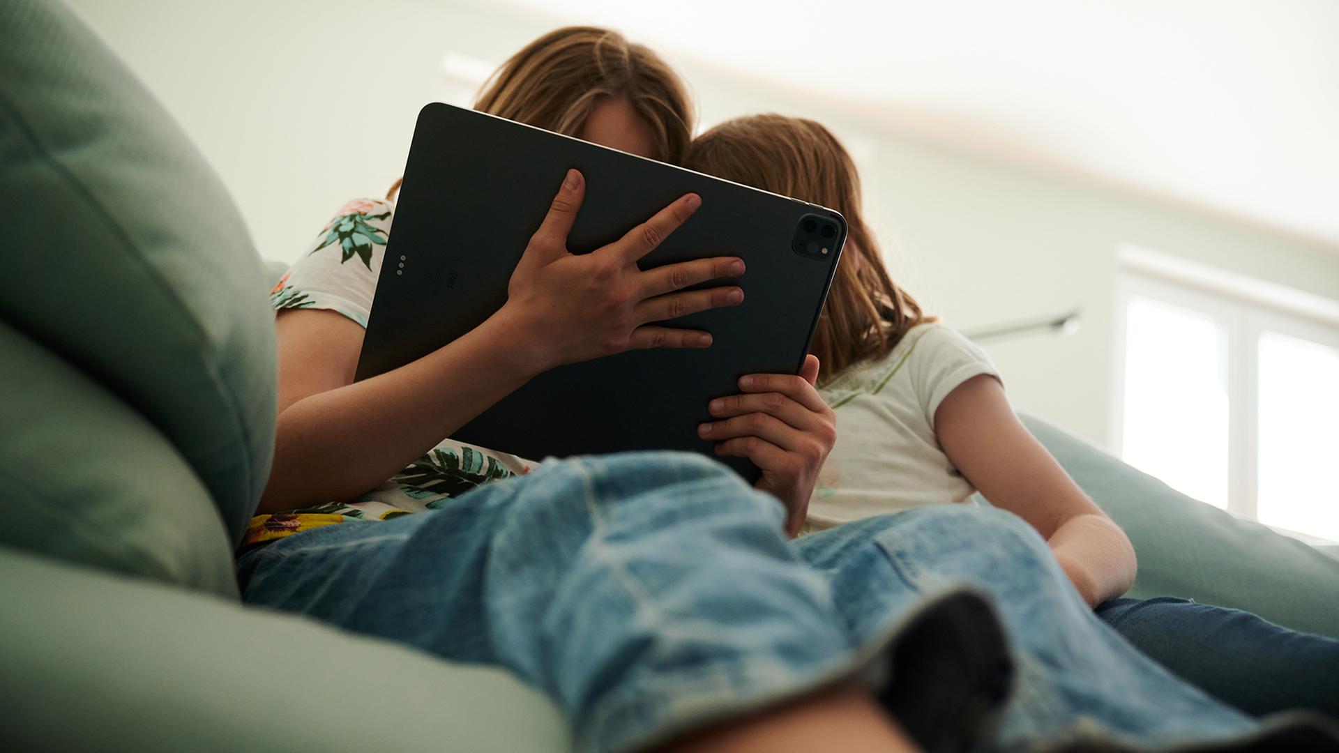 Zwei Kinder sitzen mit einem Tablet auf dem Sofa. | dpa