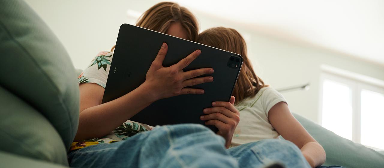 Zwei Kinder sitzen mit einem Tablet auf dem Sofa.
