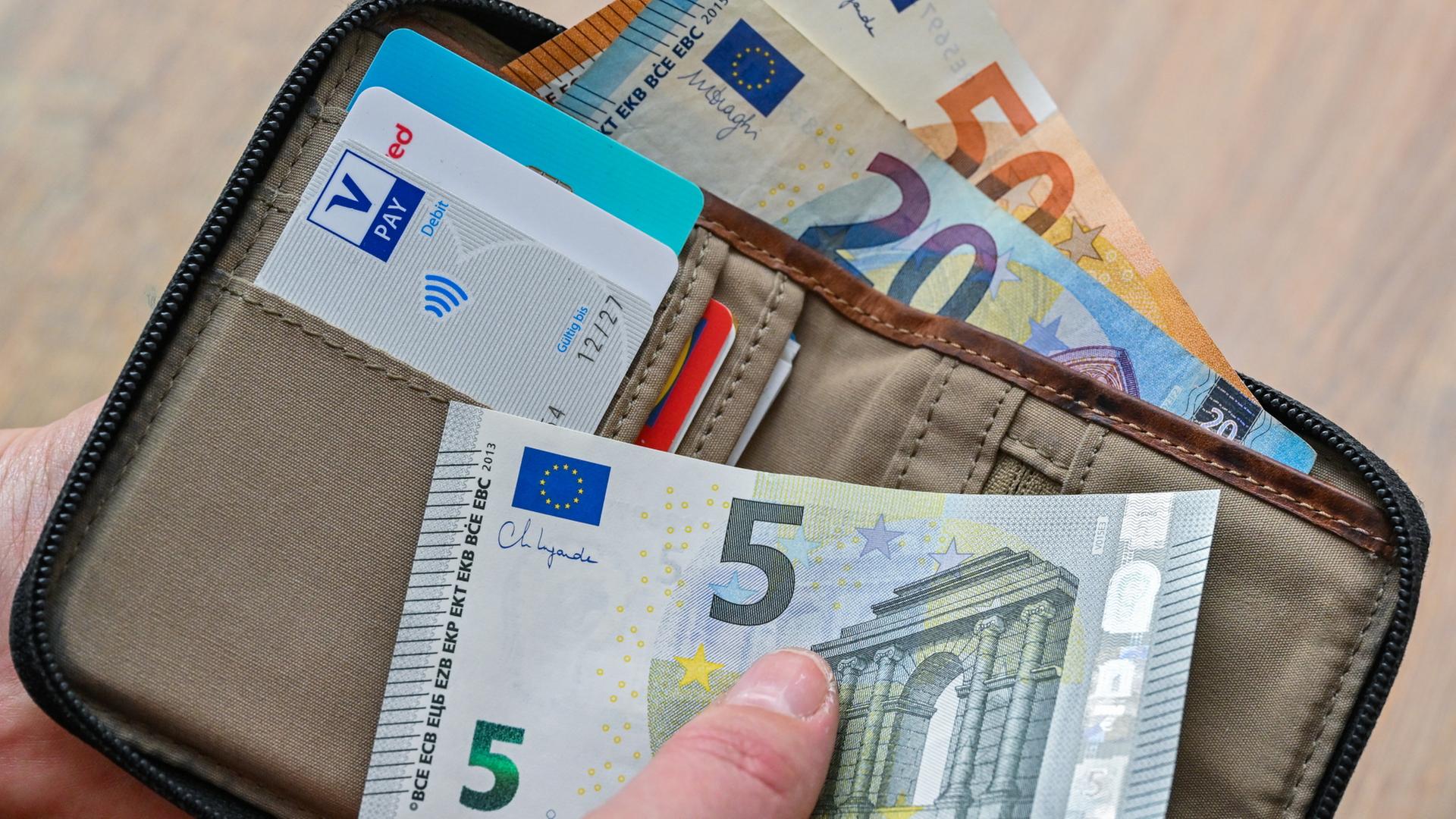 Eine Frau hält in ihrer Hand eine Brieftasche mit Geld und Bankkarten. | dpa