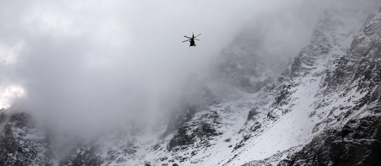 Ein Hubschrauber der Bergrettung fliegt über ein mit Schnee bedecktes Gebirge.