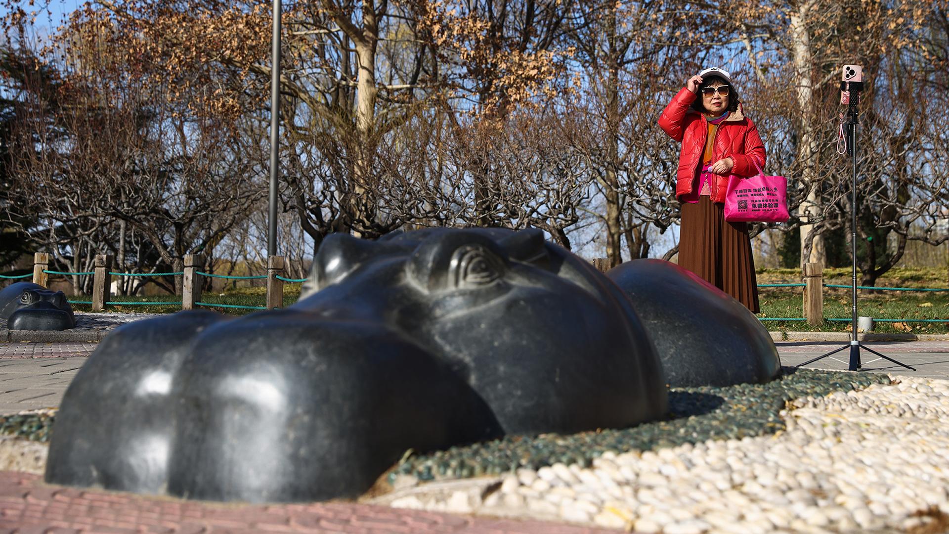 Eine Frau steht neben einer Flusspferd-Figur in einem Park in Peking. | EPA