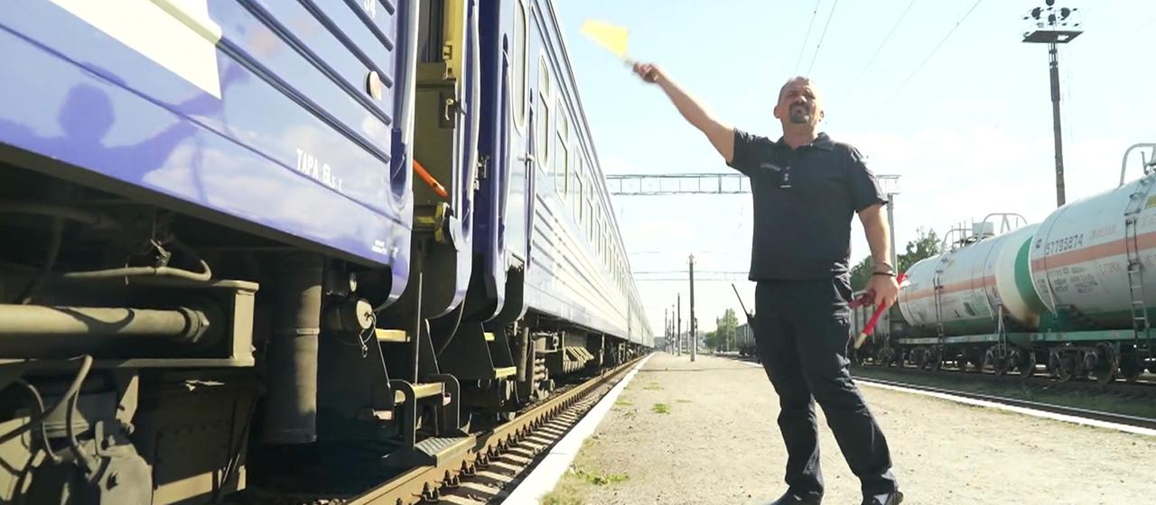 Ein Zugbegleiter schwenkt eine Fahne an einem Bahnsteig.