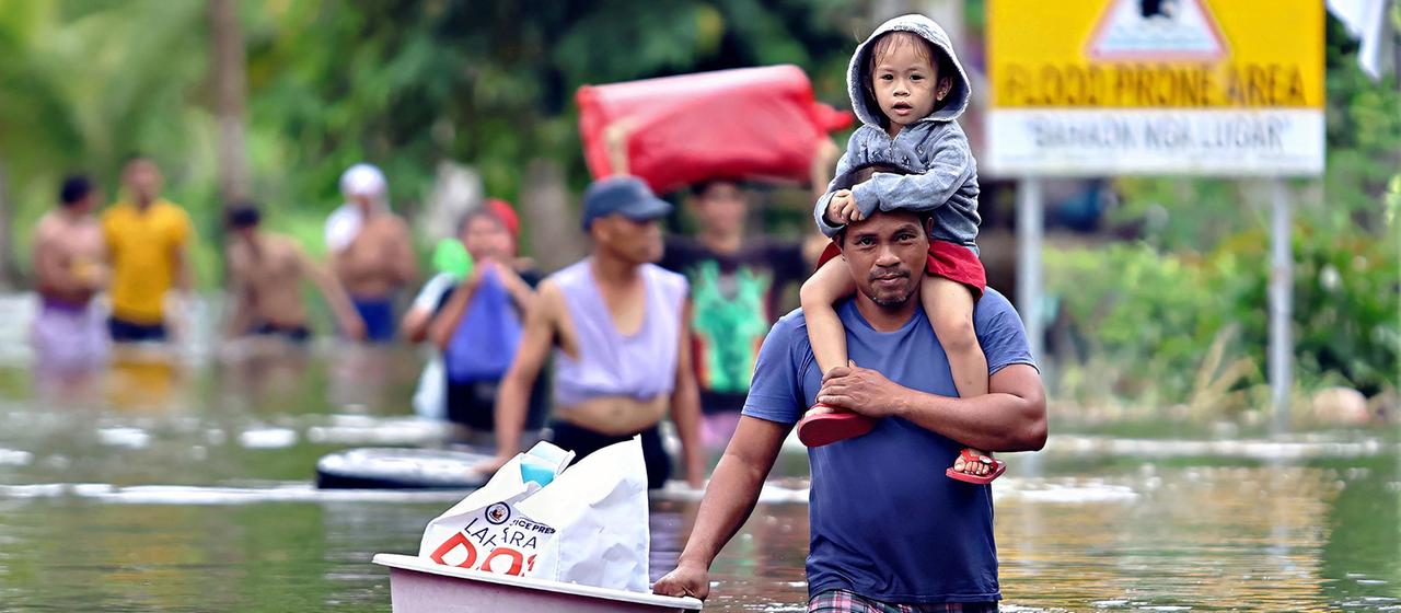 Menschen waten durch eine überflutete Straße.