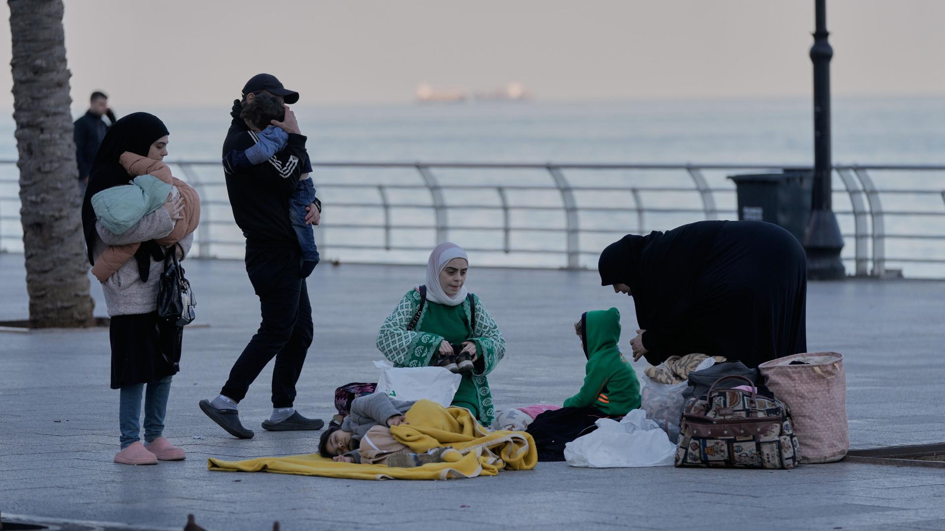 Eine vertriebene Familie sitzt auf einem Bürgersteig an der Corniche von Beirut.  | Bilal Hussein/AP/dpa
