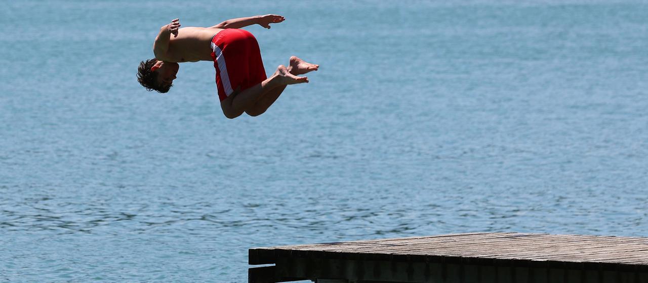 Ein junger Mann springt von einem Steg in das kühle Wasser des Illasbergsees.