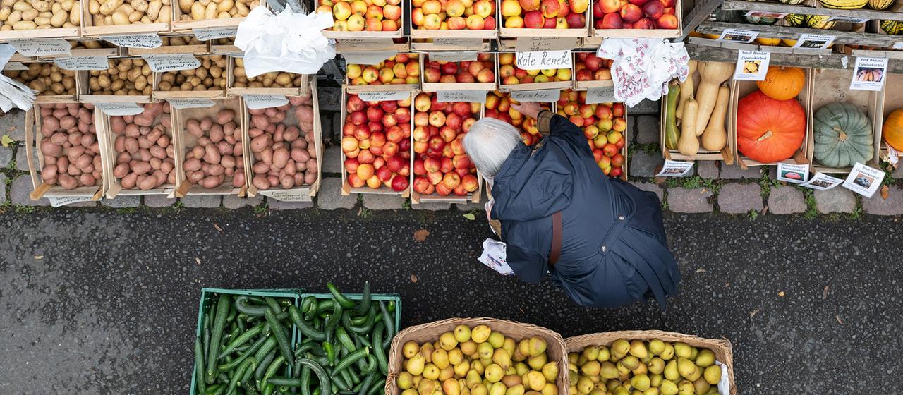 Eine Frau steht auf einem Wochenmarkt an einem Stand mit Obst und Gemüse.
