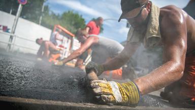 Straßenarbeiter asphaltieren in der Sommerhitze einen Teil der Fahrbahn.