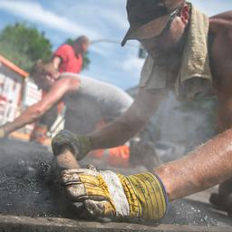 Straßenarbeiter asphaltieren in der Sommerhitze einen Teil der Fahrbahn.