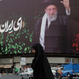 Eine Frau geht in einer Straße an einem großen Bild von Ali Chamenei in Teheran vorbei.