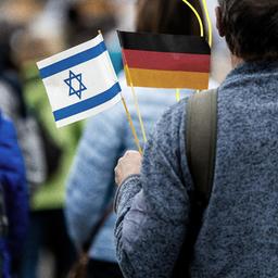 Ein Teilnehmer einer proisraelischen Kundgebung hält kleine Flaggen Israels und Deutschlands in der Hand.