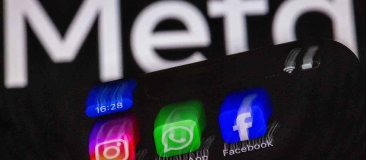 Der Meta-Schriftzug, davor ein Handy mit den Symbolen von Facebook, Instagram und WhatsApp