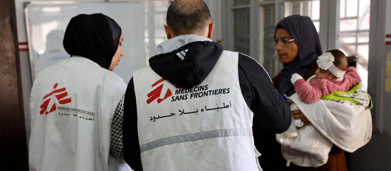 A woman with a baby in her arms talks to two Médecins Sans Frontières employees in Gaza