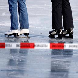 Schlittschuhläufer stehen auf einem zugefrorenen See hinter einem Absperrband.