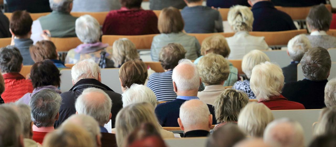 Zahlreiche Rentner sitzen auf Bänken 