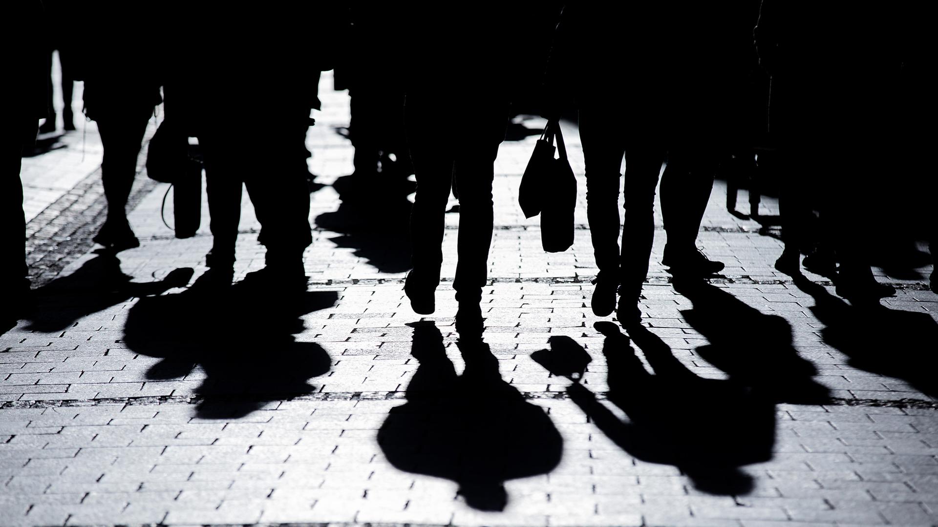 Passanten gehen in starkem Gegenlicht durch eine Fußgängerzone und werfen Schatten auf den Asphalt.  | picture alliance/dpa