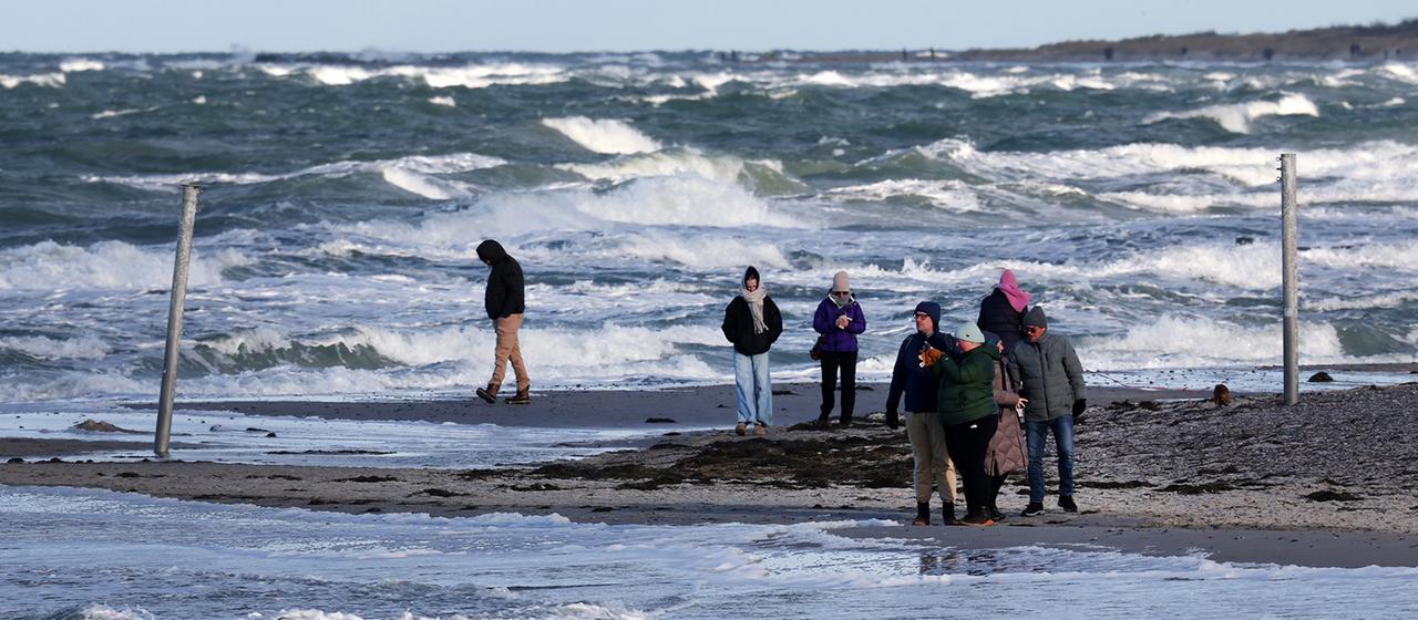 People walk on a beach in strong surf.