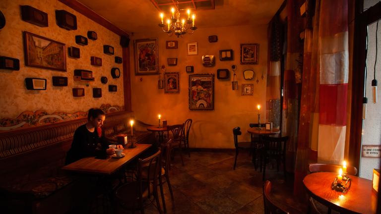 Eine Frau sitzt in einem mit Kerzen beleuchteten Restaurant, während eines Stromausfalles (Archivbild).