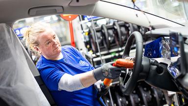 Eine Mitarbeiterin montiert in einem Fahrzeug im VW Werk ein Lenkrad.