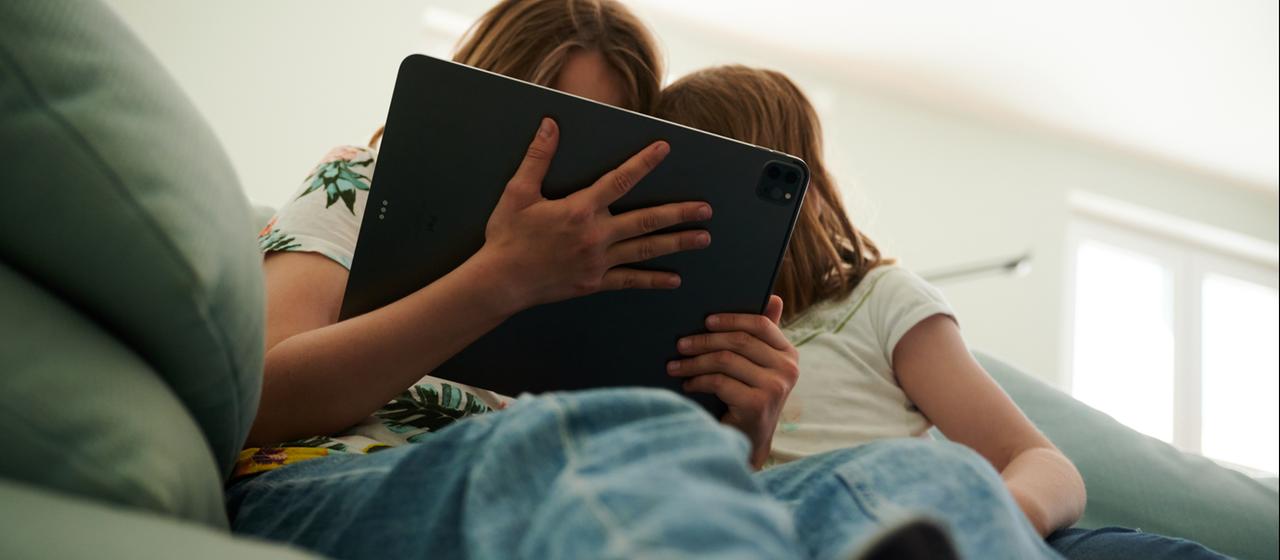Zwei Kinder sitzen auf einem Sofa und schauen auf ein Tablet