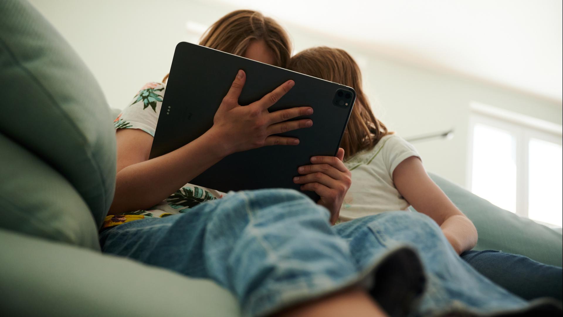 Zwei Kinder sitzen auf einem Sofa und schauen auf ein Tablet | dpa