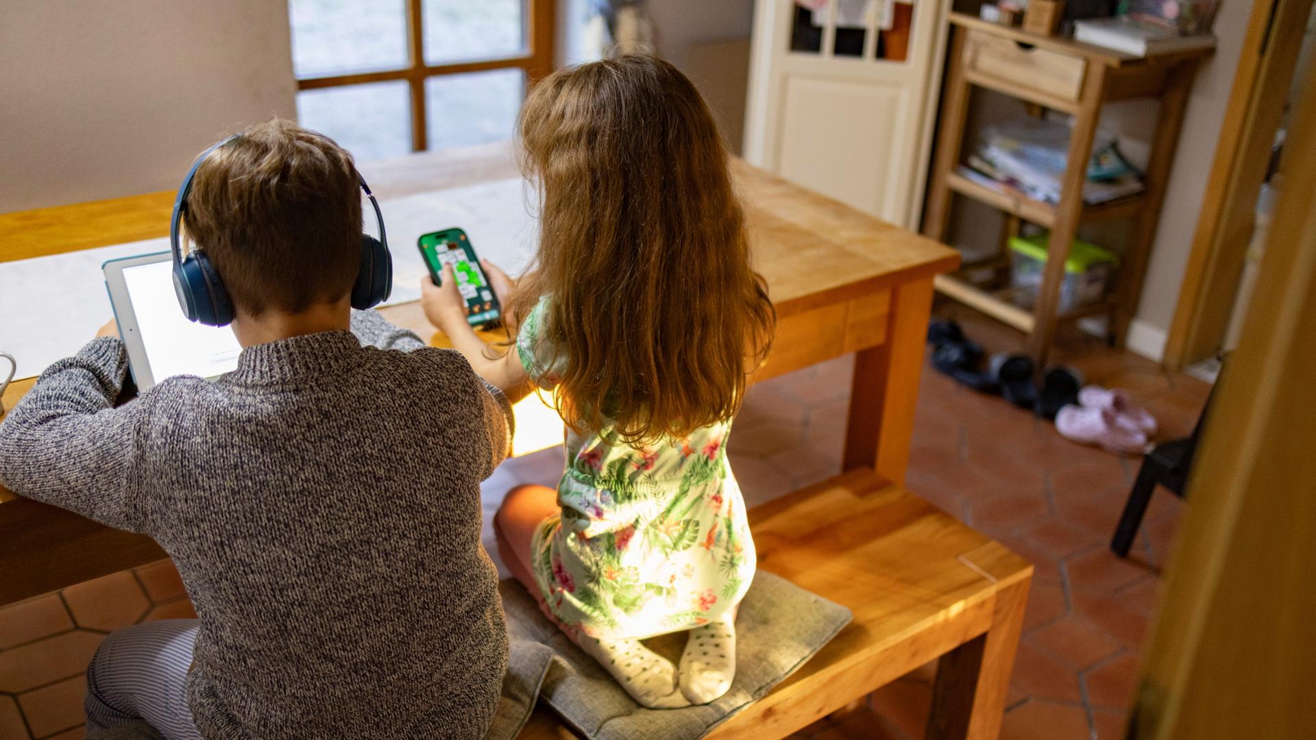 Zwei Kinder sitzen an einem Tisch und schauen auf ein Tablet und ein Handy. | ARD-aktuell / Henning Retzlaff