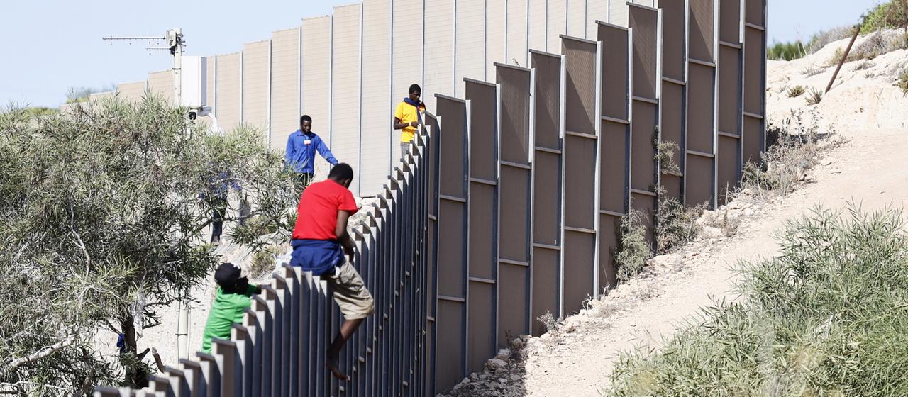 Migranten klettern über einen Zaun auf der Insel Lampedusa.