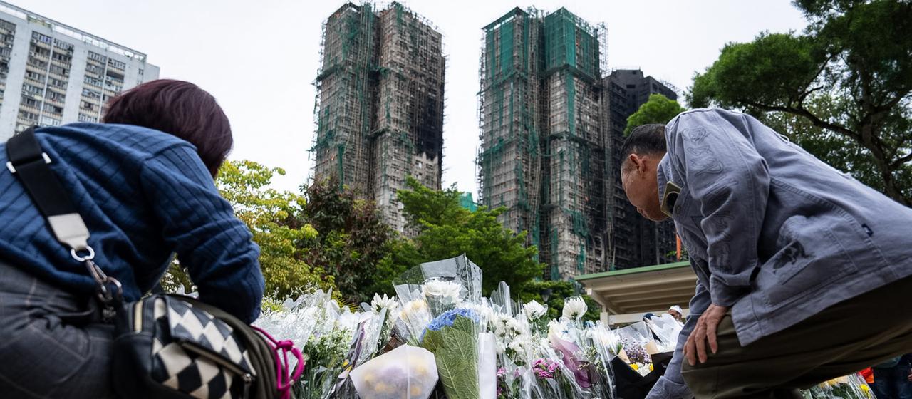Menschen legen Blumen vor den zerstörten Hochhäusern in Hongkong nieder